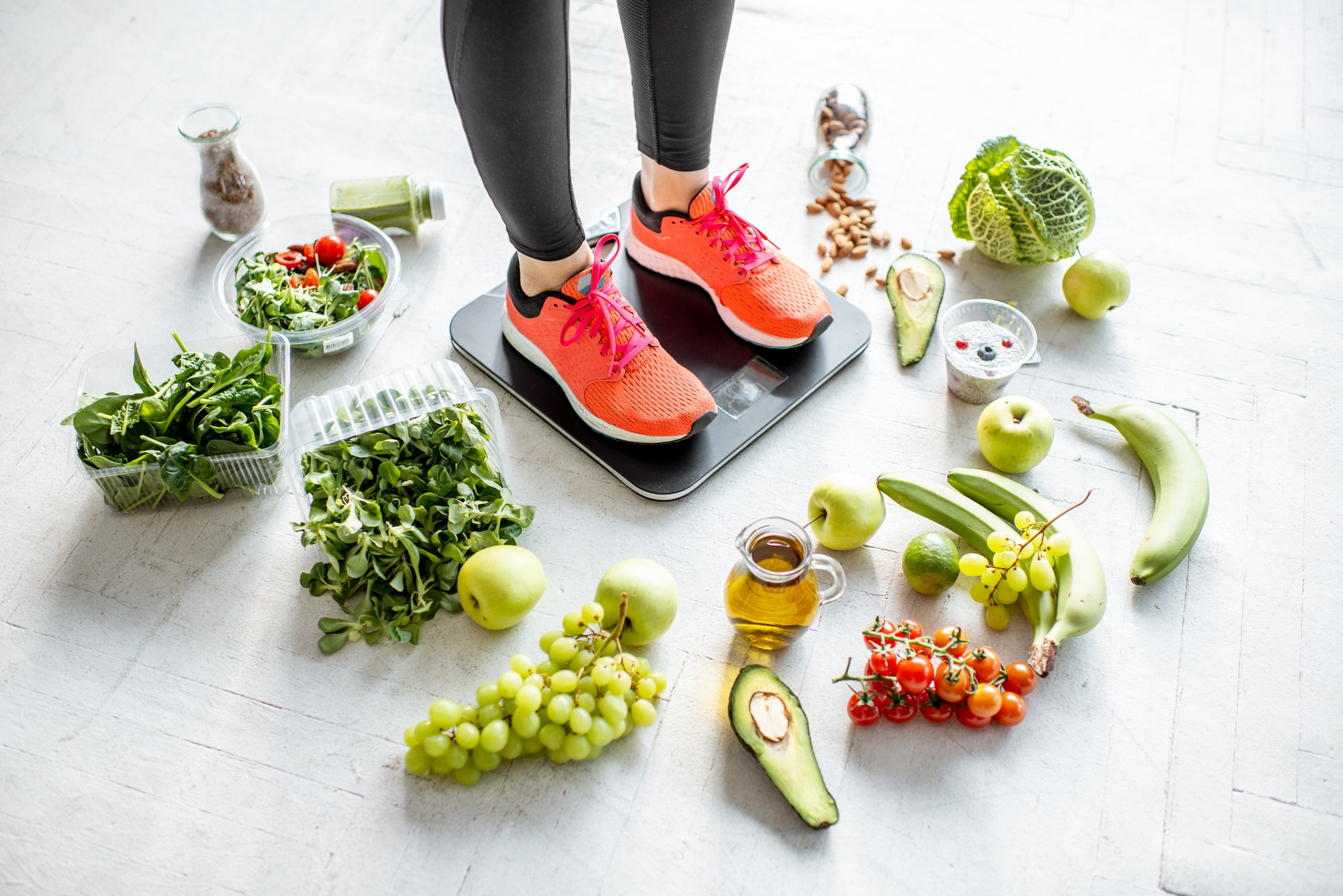 Sports woman weighing with healthy food around